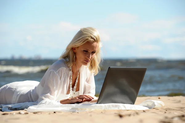 Bir dizüstü bilgisayar ile bir plajda mutlu sarışın kadın — Stok fotoğraf