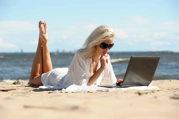 Mulher loira feliz em uma praia com um laptop — Fotografia de Stock