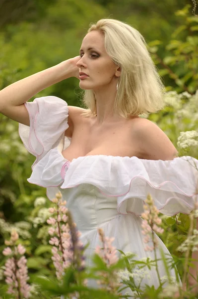 Menina em um vestido branco no campo entre as flores — Fotografia de Stock