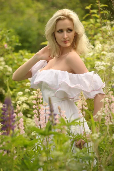Menina em um vestido branco no campo entre as flores — Fotografia de Stock