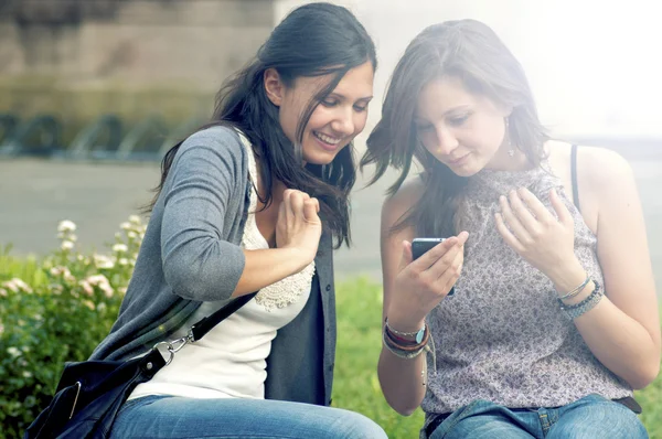 Dos chicas mientras hablan mirando el teléfono celular — Foto de Stock