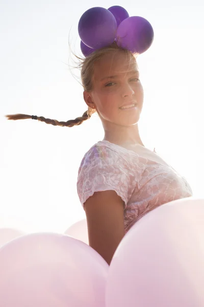 Menina cercada por balões pelos raios de luz solar — Fotografia de Stock