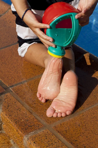 Child´s legs with watering can on the swimming pool background — Stock Photo, Image