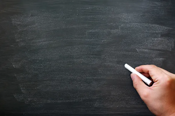 Vlekkerig schoolbord achtergrond met een hand met krijt schrijven. — Stockfoto