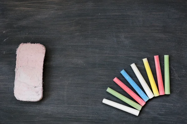 Kleurrijke krijt en gum op een lege vlekkerig schoolbord — Stockfoto