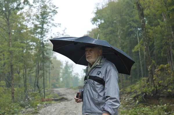 Senior geht mit Regenschirm spazieren — Stockfoto