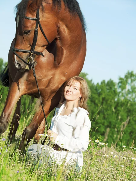 Linda chica con su caballo en el campo de flores — Foto de Stock