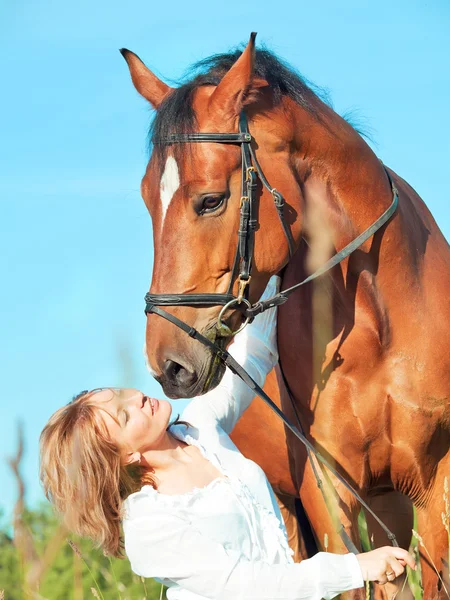 Hermosa chica con caballo de bahía en el fondo del cielo azul — Foto de Stock