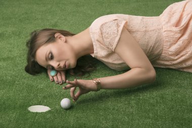 Girl lying on grass with golf ball, she hits clipart