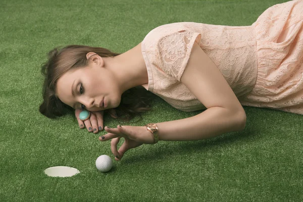 Menina deitada na grama com bola de golfe, ela bate — Fotografia de Stock