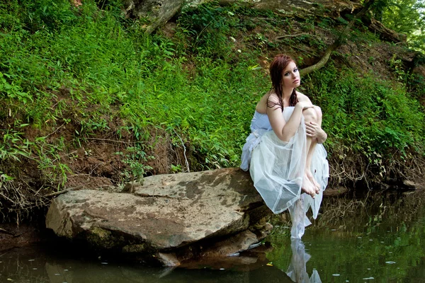 Mulher sentada em uma rocha junto ao rio — Fotografia de Stock