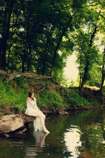 Bride sitting on riverbank — Stock Photo, Image
