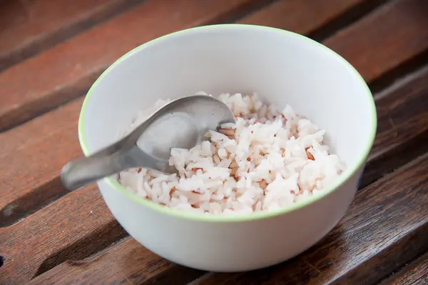 stock image White and brown steamed rice in white round bowl and spoon on wood pattern background