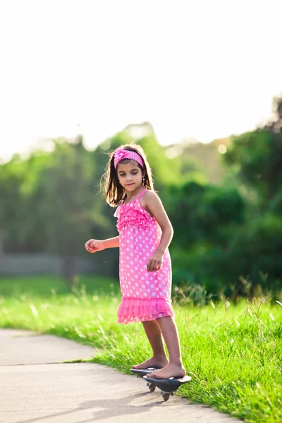 Молодая девушка в розовом платье катается на скейтборде — стоковое фото