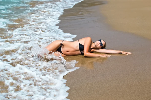 Kvinna liggande på våta sanden mot havet och blå himmel — Stockfoto