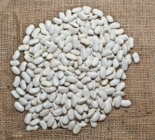 Bílé fazole, roztroušených na pytlovina — Stock fotografie
