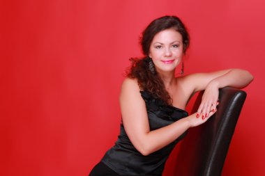 Stüdyo resmi üzerinde kırmızı zemin üzerine kapalı stüdyo oturumdaki moda siyah elbiseli genç kadın