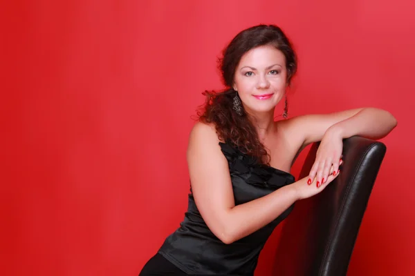 Imagem de estúdio da jovem mulher em vestido preto na sessão de moda no estúdio interior sobre fundo vermelho — Fotografia de Stock