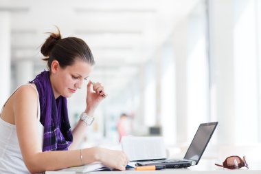 Pretty female college student studying in the university library clipart