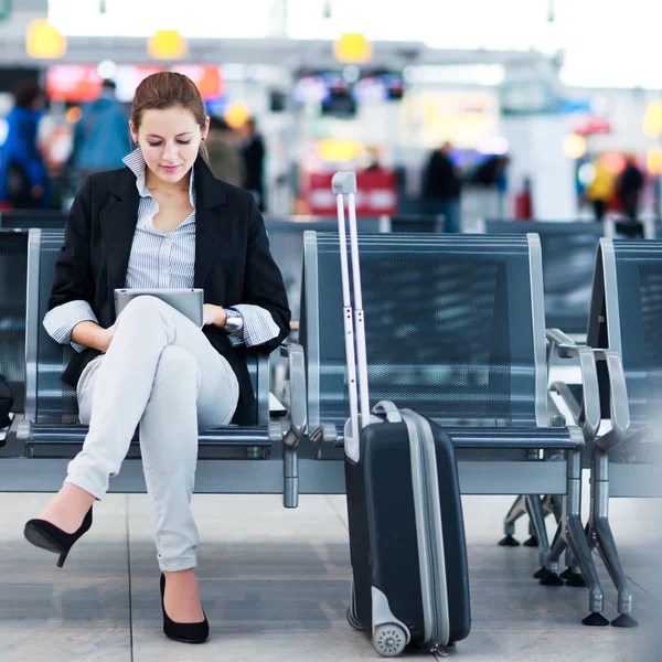 Genç bir kadın yolcu havaalanında, tablet bilgisayarını kullanarak — Stok fotoğraf