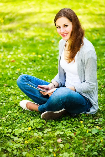 Jovem mulher usando seu computador tablet enquanto relaxa ao ar livre — Fotografia de Stock