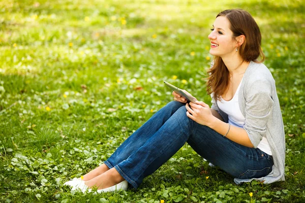 Молода жінка використовує свій планшетний комп'ютер, розслабляючись на відкритому повітрі — стокове фото