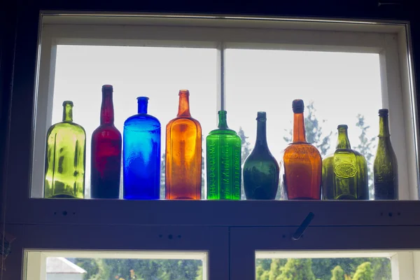 Colored bottles standing on windowsill in line — Stock Photo, Image