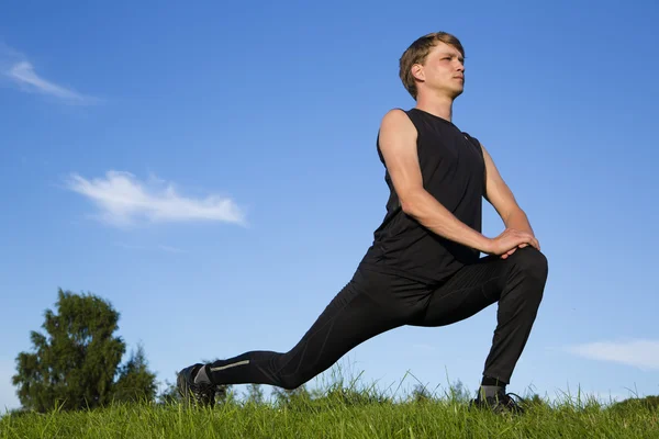 Sportsman making exercise movements to stretch legs — Stock Photo, Image