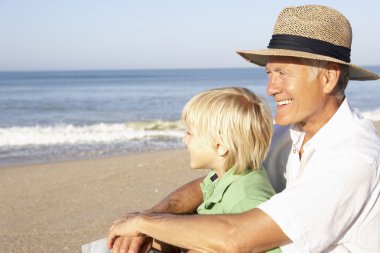 Grandfather with child on beach relaxing clipart