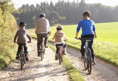 Young parents with children ride bikes in park clipart