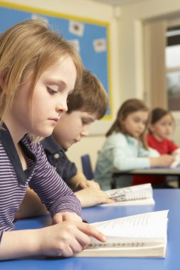 Schoolgirl Reading Book In Classroom clipart