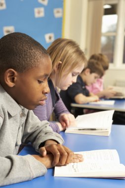 Schoolboy Reading Book In Classroom clipart