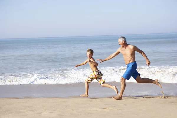 Grandfather chasing young boy on beach — Stockfoto