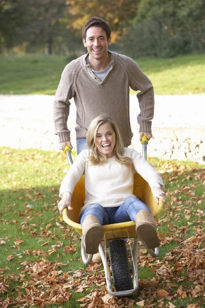 男人在独轮车上推妻子通过秋天的树叶 — 图库照片