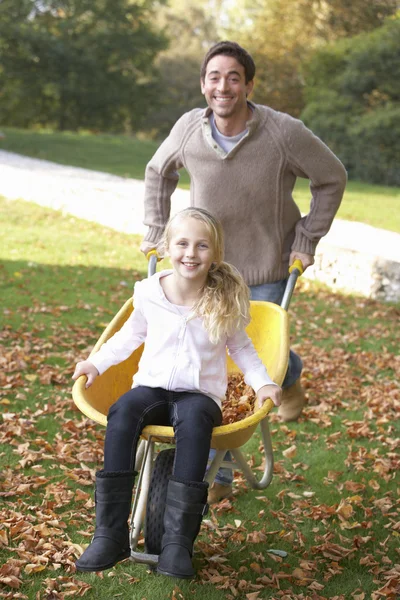 Pai empurrando criança através de folhas de outono no carrinho de mão — Fotografia de Stock