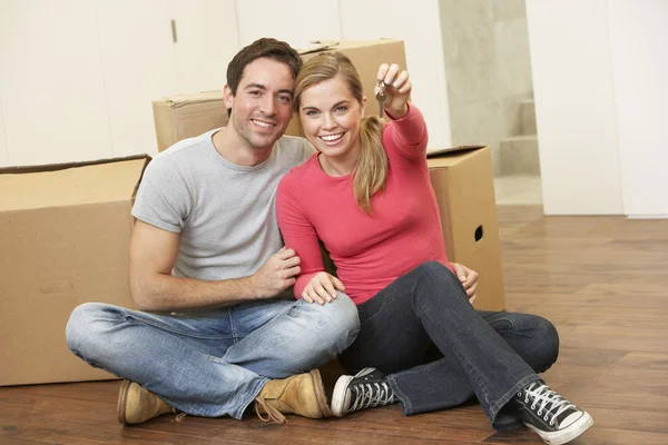 Jeune couple assis sur le sol autour de boîtes tenant la clé dans la main — Photo