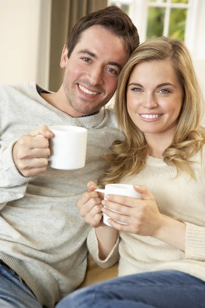 Молода пара сидить і розслабляється на дивані з чашкою в руці — стокове фото