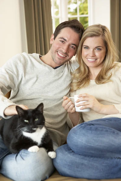 젊은 부부 잔 함께 소파에 고양이 함께 손에 앉아 — 스톡 사진