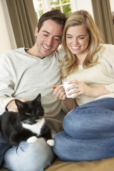 Jeune couple assis avec chat sur canapé avec tasse à la main — Photo