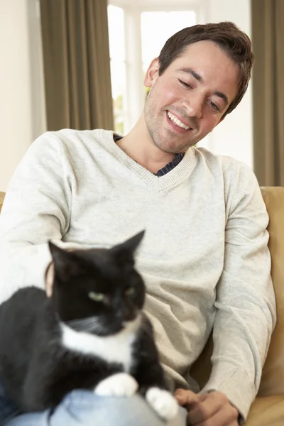 Glücklicher junger Mann mit Katze auf Sofa sitzend — Stockfoto