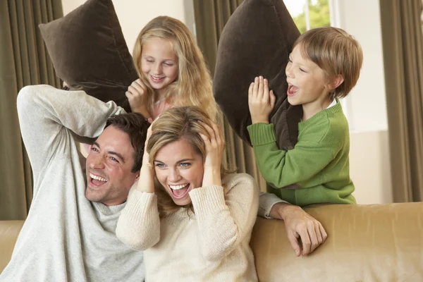Feliz jovem família se divertindo com travesseiros no sofá — Fotografia de Stock