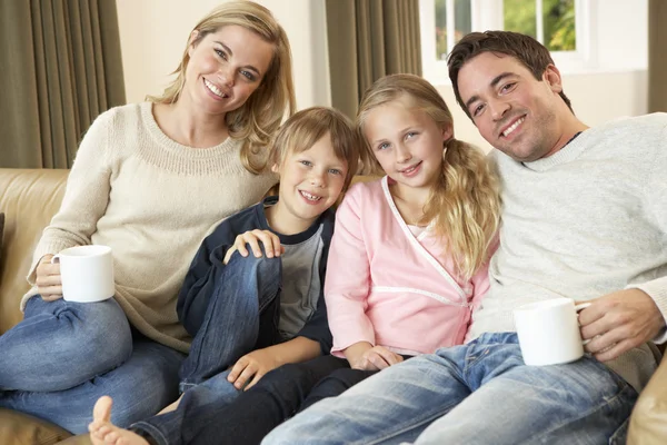 Счастливая молодая семья сидит на диване, держа чашки — стоковое фото