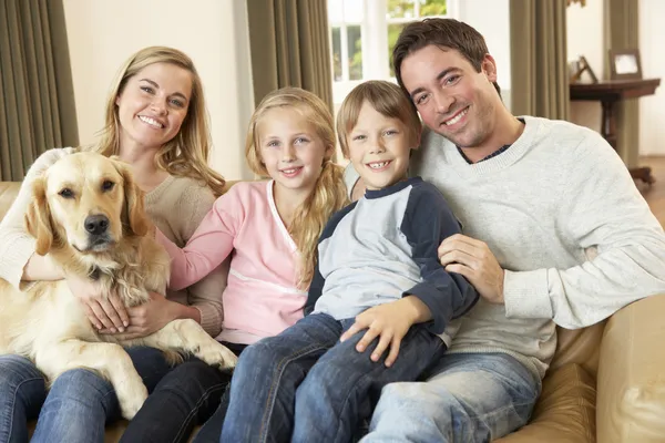 Happy young family sitting on sofa holding a dog — Stock Photo, Image
