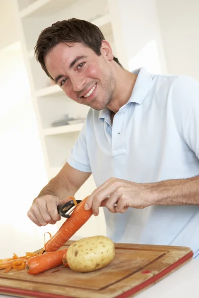 快乐的年轻男人剥皮在厨房里的蔬菜 — 图库照片