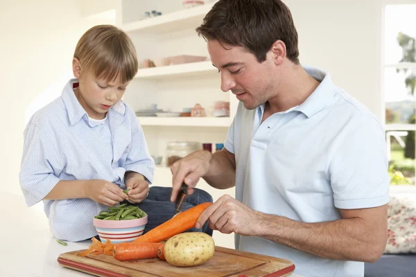 Счастливый молодой человек с мальчиком чистит овощи на кухне — стоковое фото