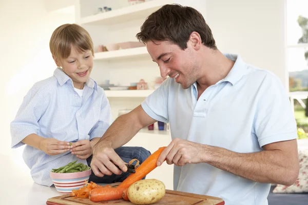 Happy young man with boy peeling vegetables in kitchen — Stock Photo, Image