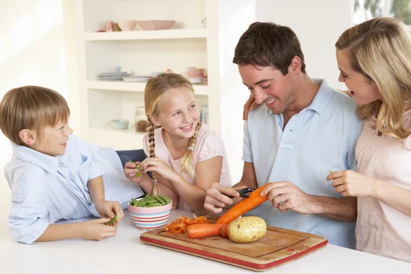 Familia feliz pelando verduras en la cocina — Foto de Stock