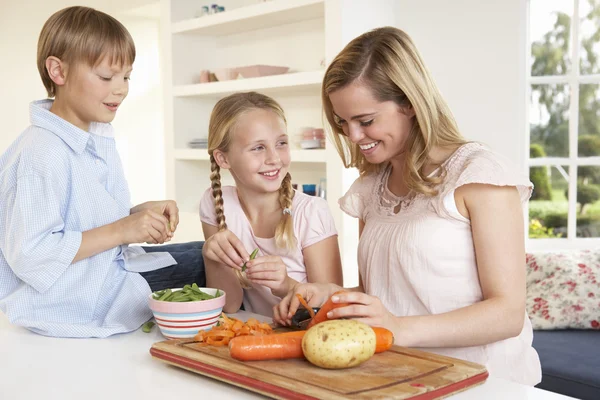 Jovem mãe com crianças descascando legumes na cozinha — Fotografia de Stock