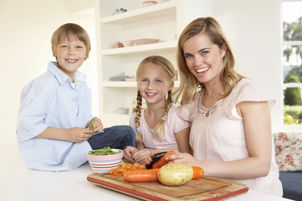 Молодая мама с детьми чистит овощи на кухне — стоковое фото