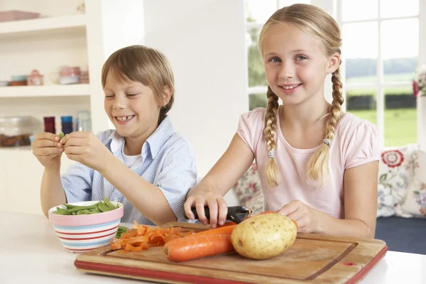 De gelukkige kinderen peeling groenten in de keuken — Stockfoto